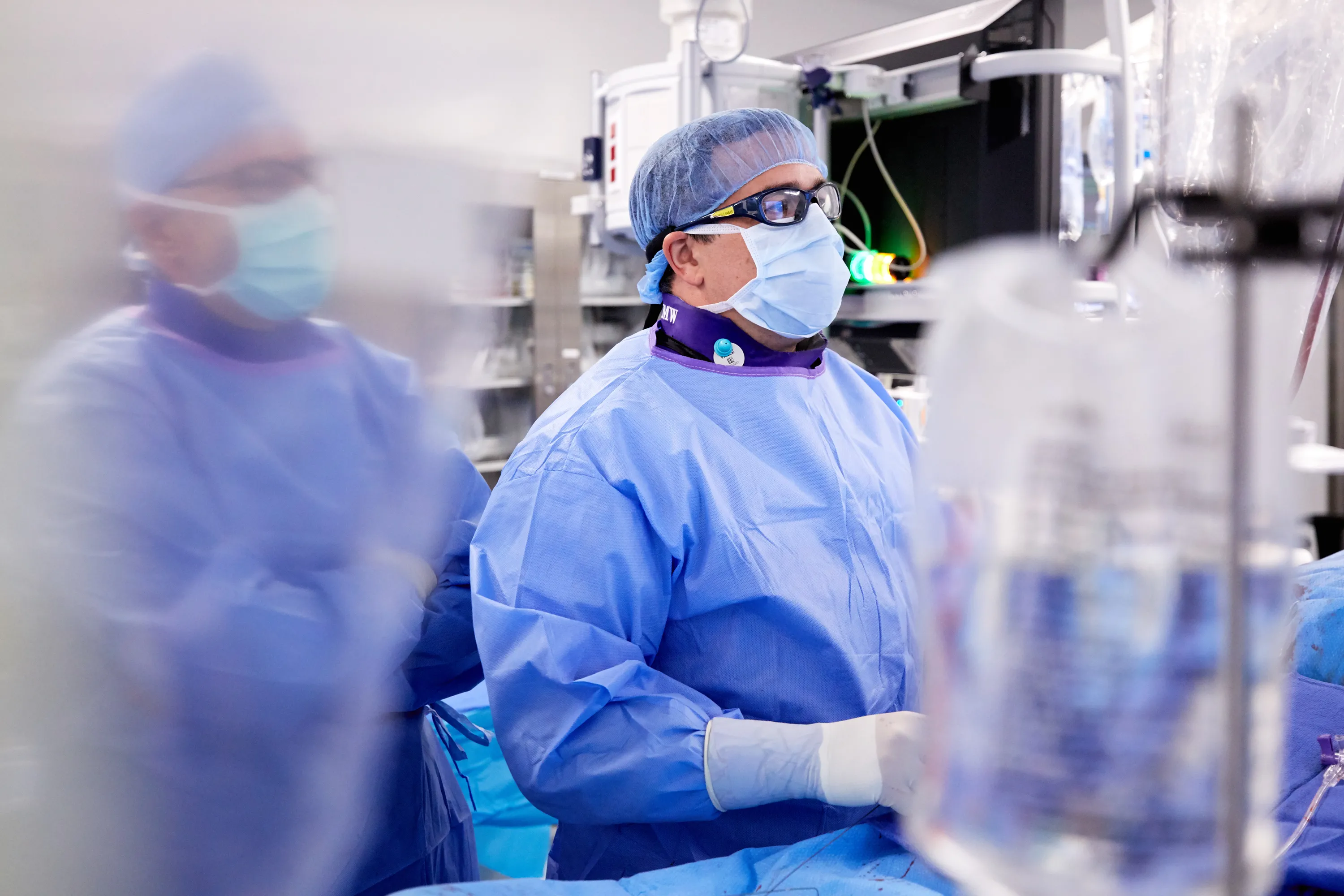 Two doctors in surgical scrubs stand in an operating room filled with surgical equipment.