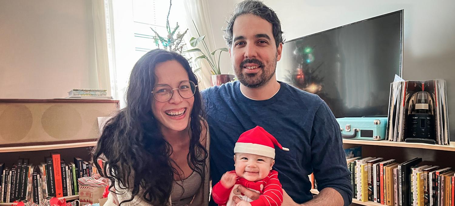 Family of Three Is Seated Together in Front of Christmas Tree and Wrapped Presents