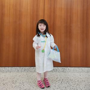 Lily stands in a hospital hallway wearing a hospital gown, pink sneakers and a play stethoscope.